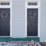 A pair of matching replacement doors freshly installed on a duplex building that’s undergoing an entryway overhaul. Two beautiful wreaths stand out against the dark-colored doors