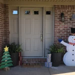 Front porch of a brick home with a beige double entry door featuring small square glass panels, flanked by sidelights, and decorated with holiday items.